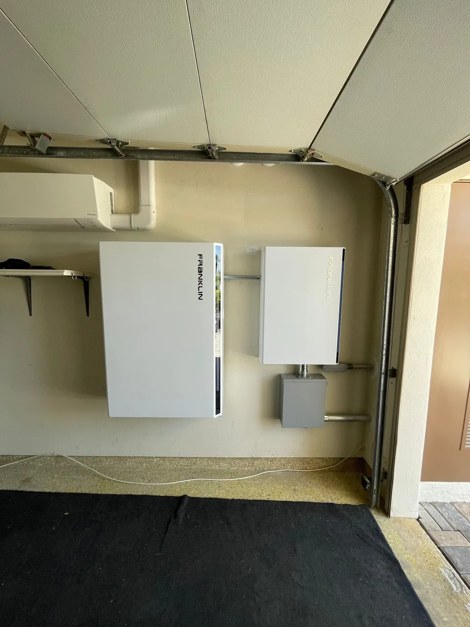A Franklin battery and control unit mounted beside a garage opening beneath a mini-split air conditioner.