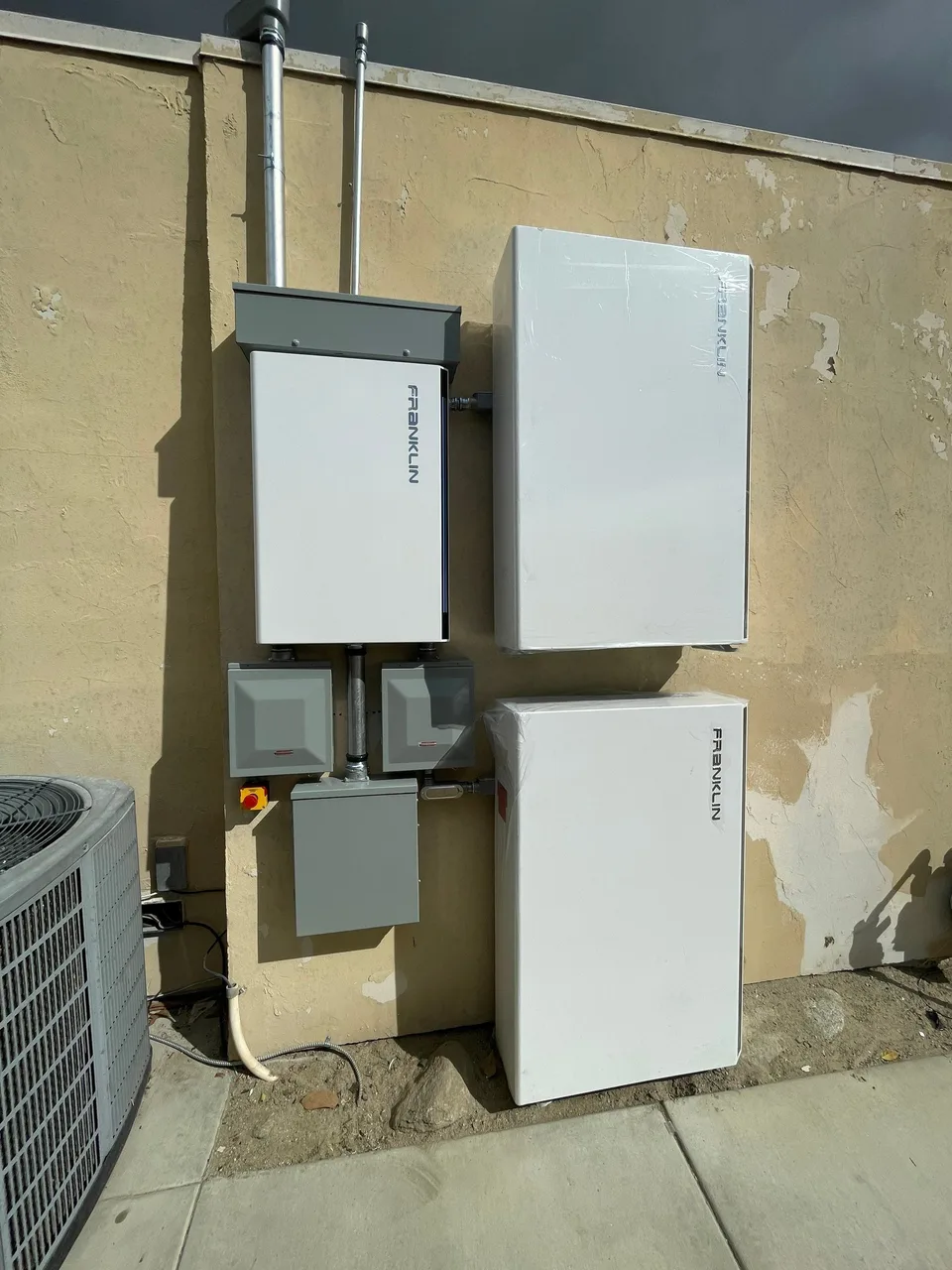 Two Franklin batteries mounted vertically on an exterior stucco wall beside a Franklin control unit.
