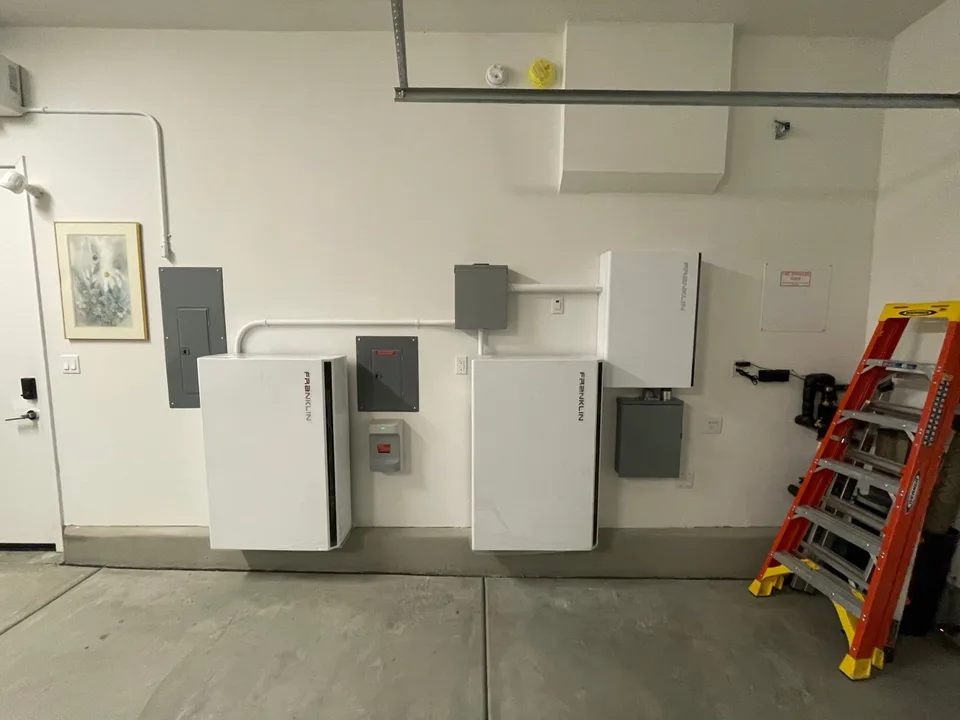 Two Franklin batteries and a Franklin control unit connected to electrical panels along a garage wall.
