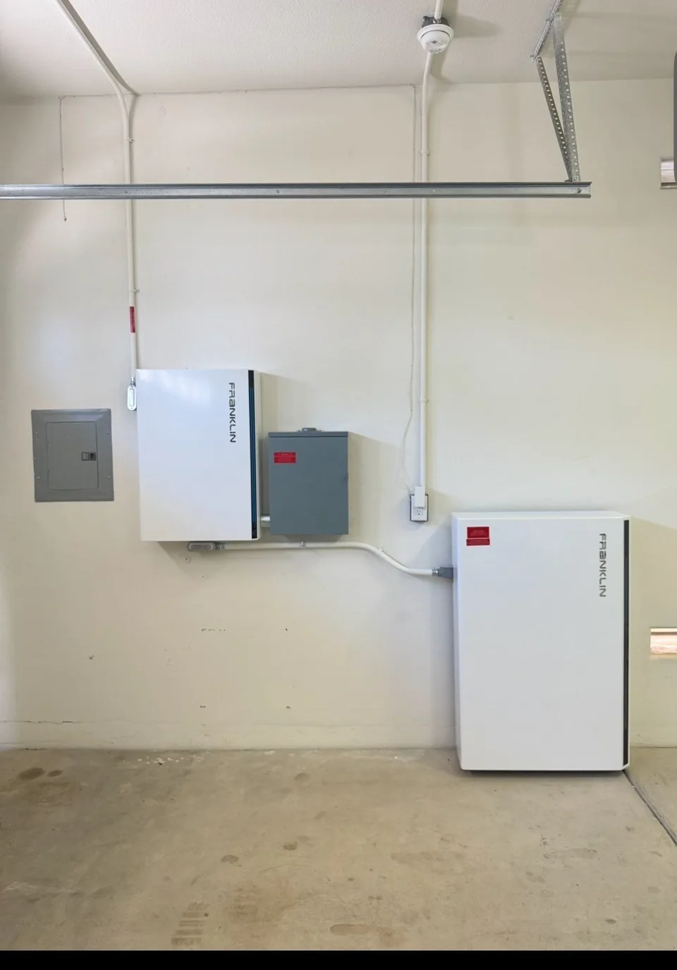 A Franklin battery near the garage floor with a wall-mounted Franklin control unit and conduit.