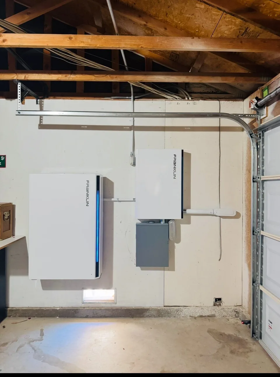A wall-mounted Franklin battery and control unit below exposed garage rafters.